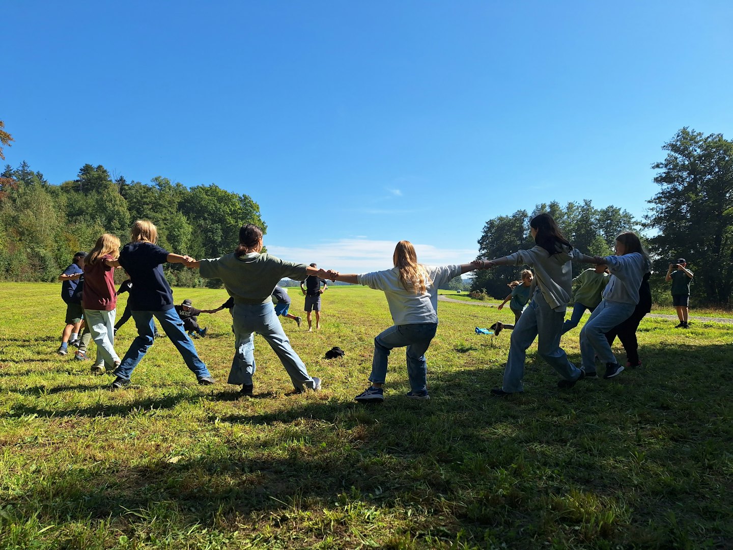 Group of people holding hands while moving across a grassy field.