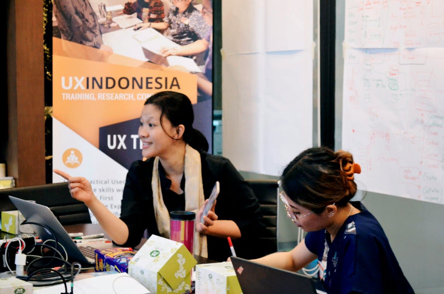 Two women collaborate during an indoor workshop with a branded banner.